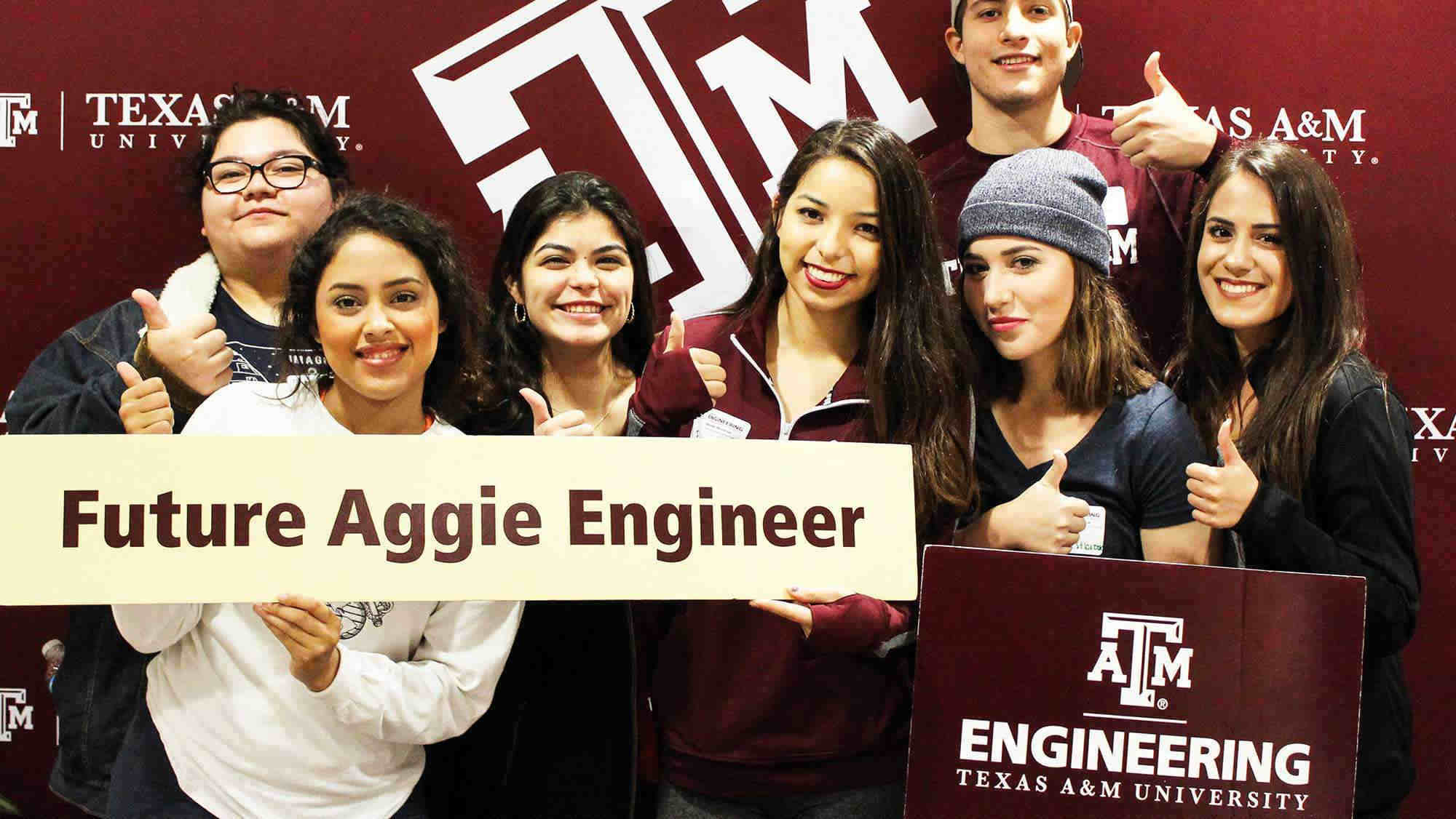 Texas A&M University in the background with seven students with their thumbs up holding a sign that says Future Aggie Engineers and Engineering Texas A&M University