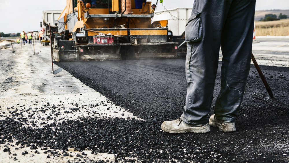 Workers and heavy machinery lay a new asphalt road 