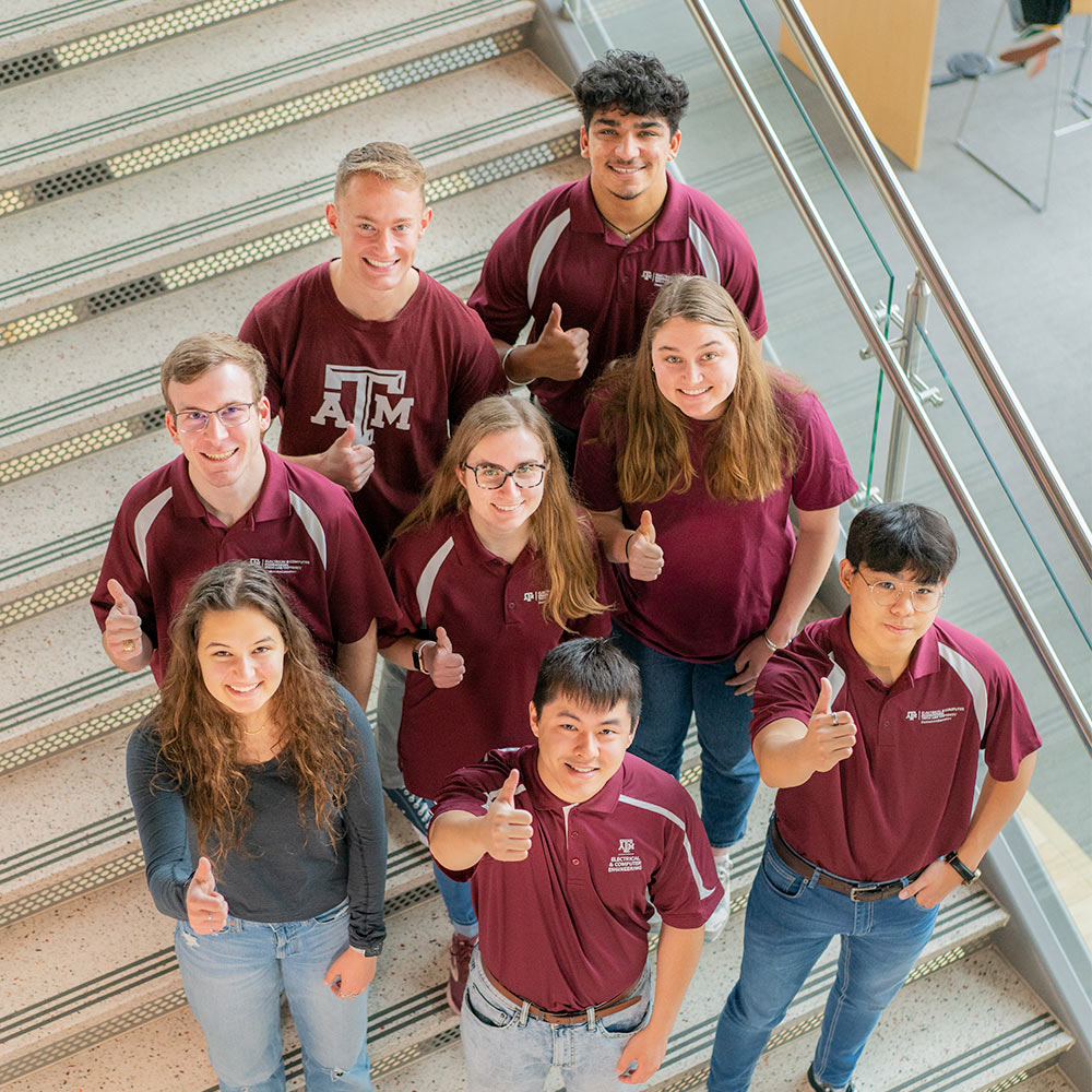 Group of students standing on stairs giving thumbs up and smiling at the camera
