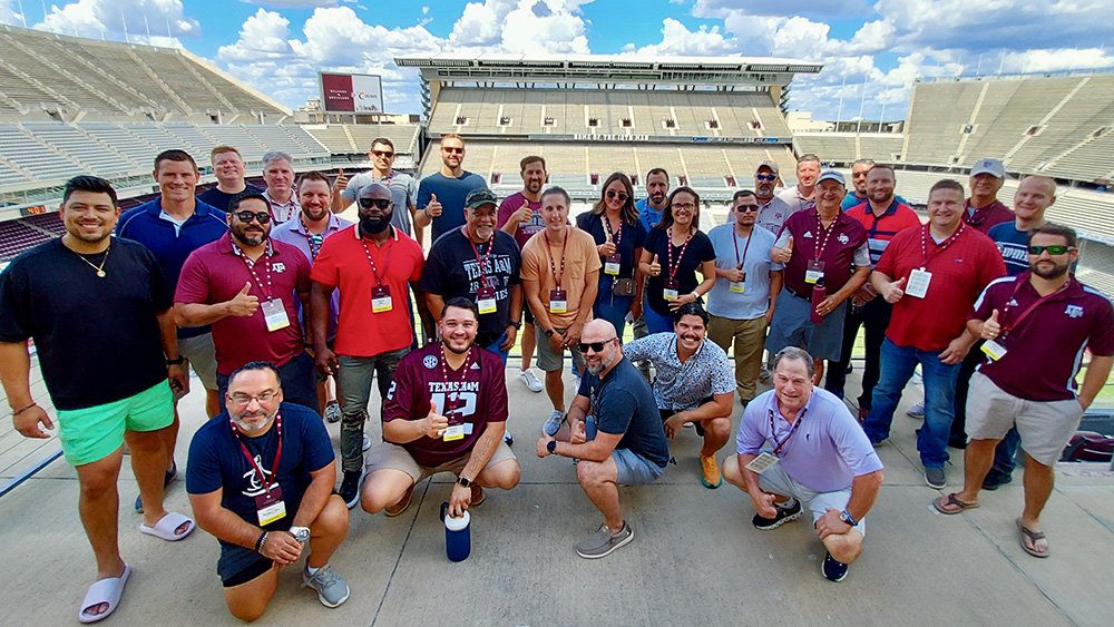 large group of older students posing and smiling while standing in Kyle Field at Texas A&amp;M University