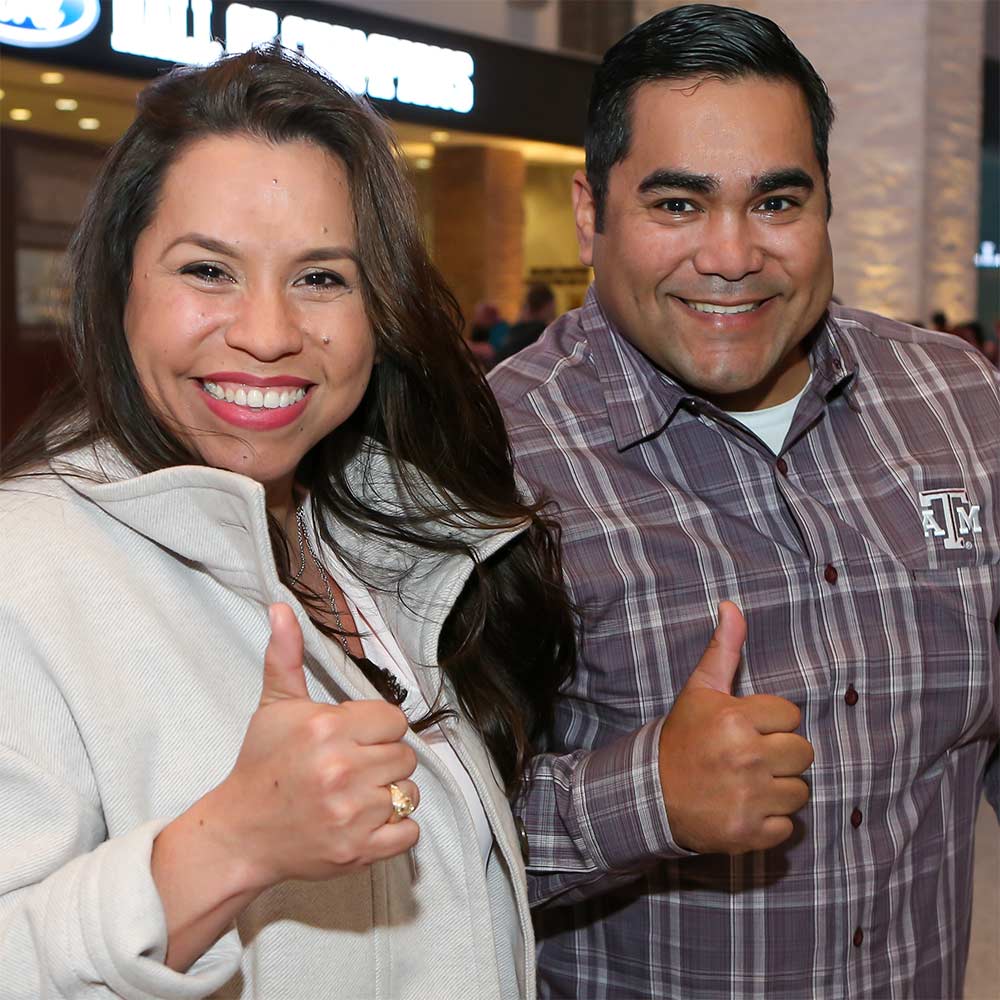 MID former graduate man and woman holding "Gig 'em" thumbs to show their Aggie rings.