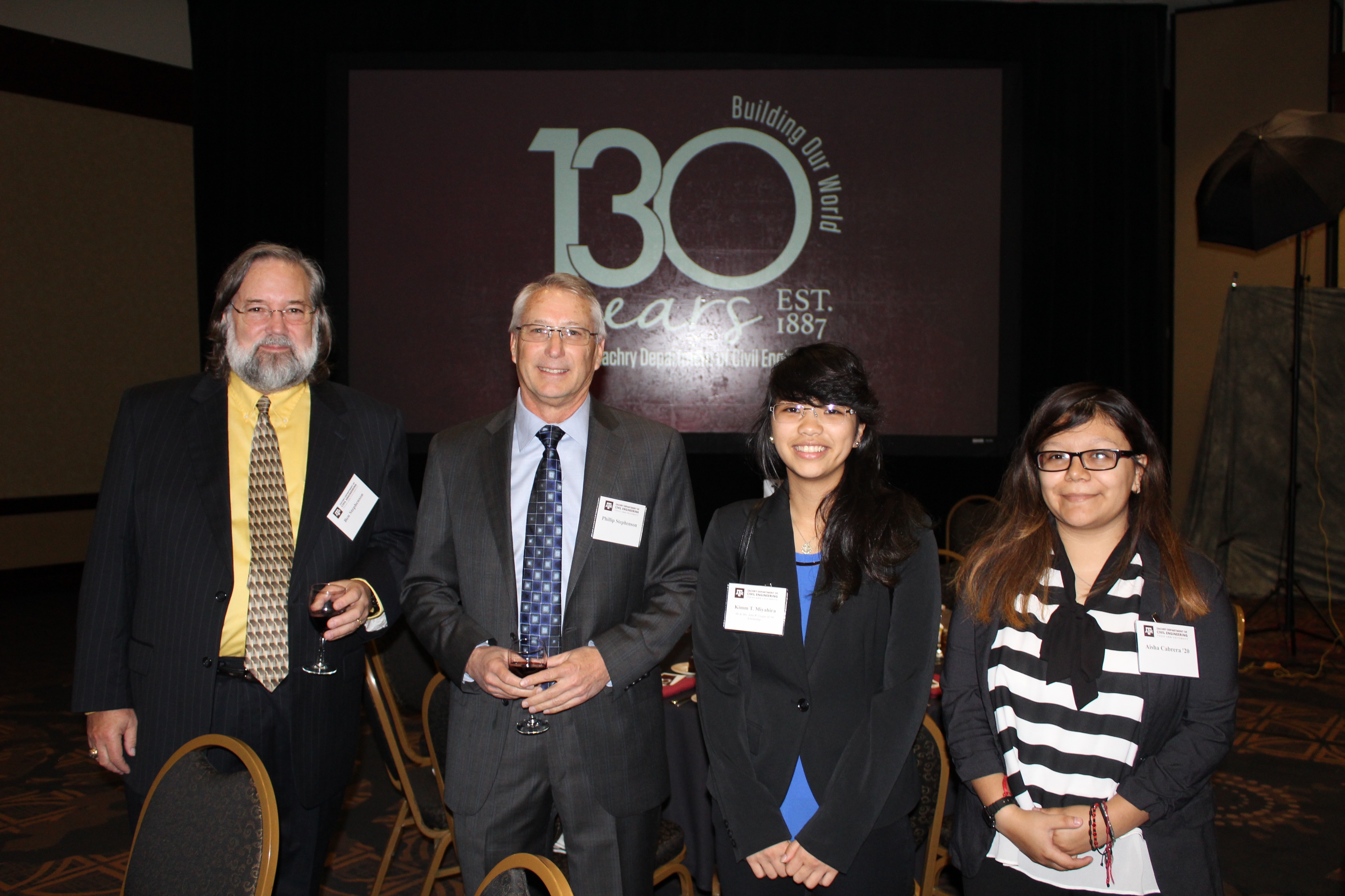 Two men and two young women in business attire at an awards banquet. Screen behind them projecting image that says "130 years: Building our world. Zachry Department of Civil Engineering."