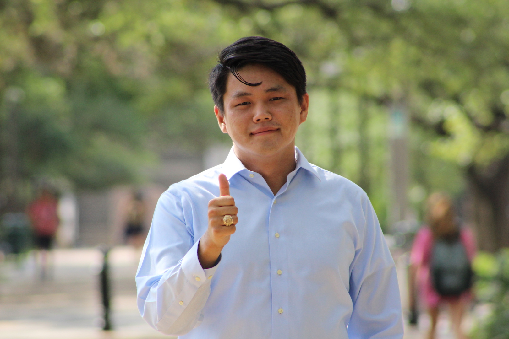 Male student of asian descent with long-sleeved white button up shirt giving thumbs up with slight smile.