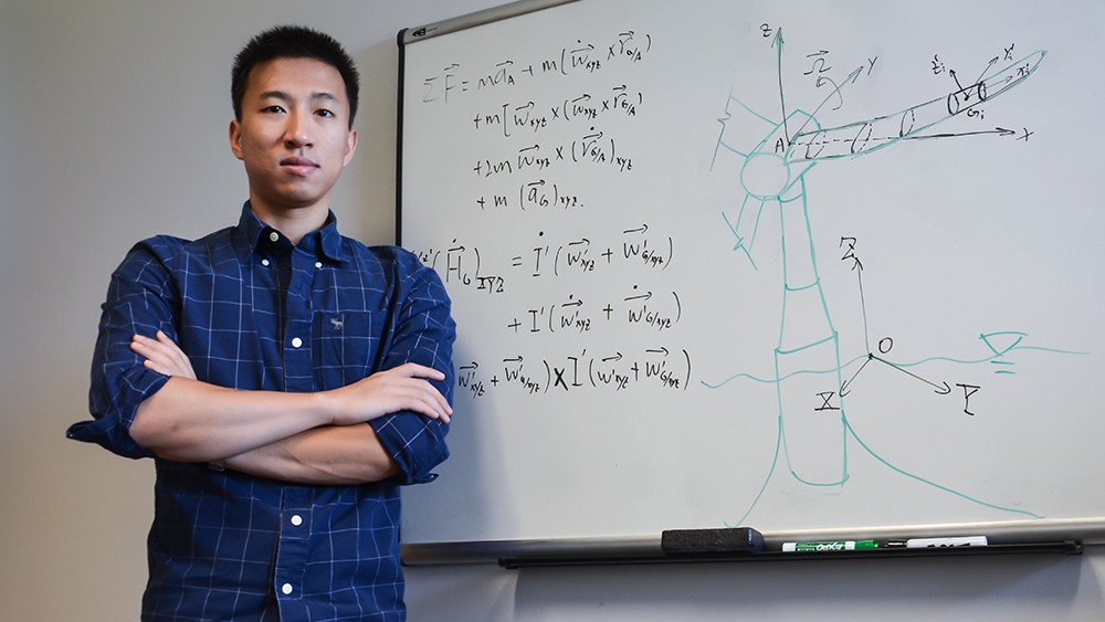 Shanran Tang stands in front of a board of equations detailing his offshore wind turbine research.