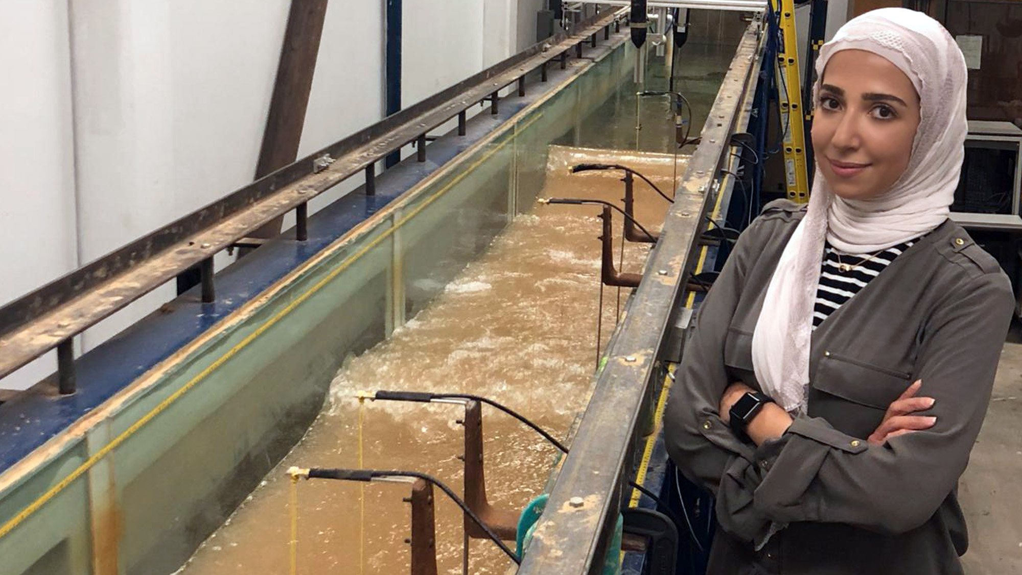 Badreyah Al-Marshed stands in front of a wave tank simulator used to conduct testing for her project.