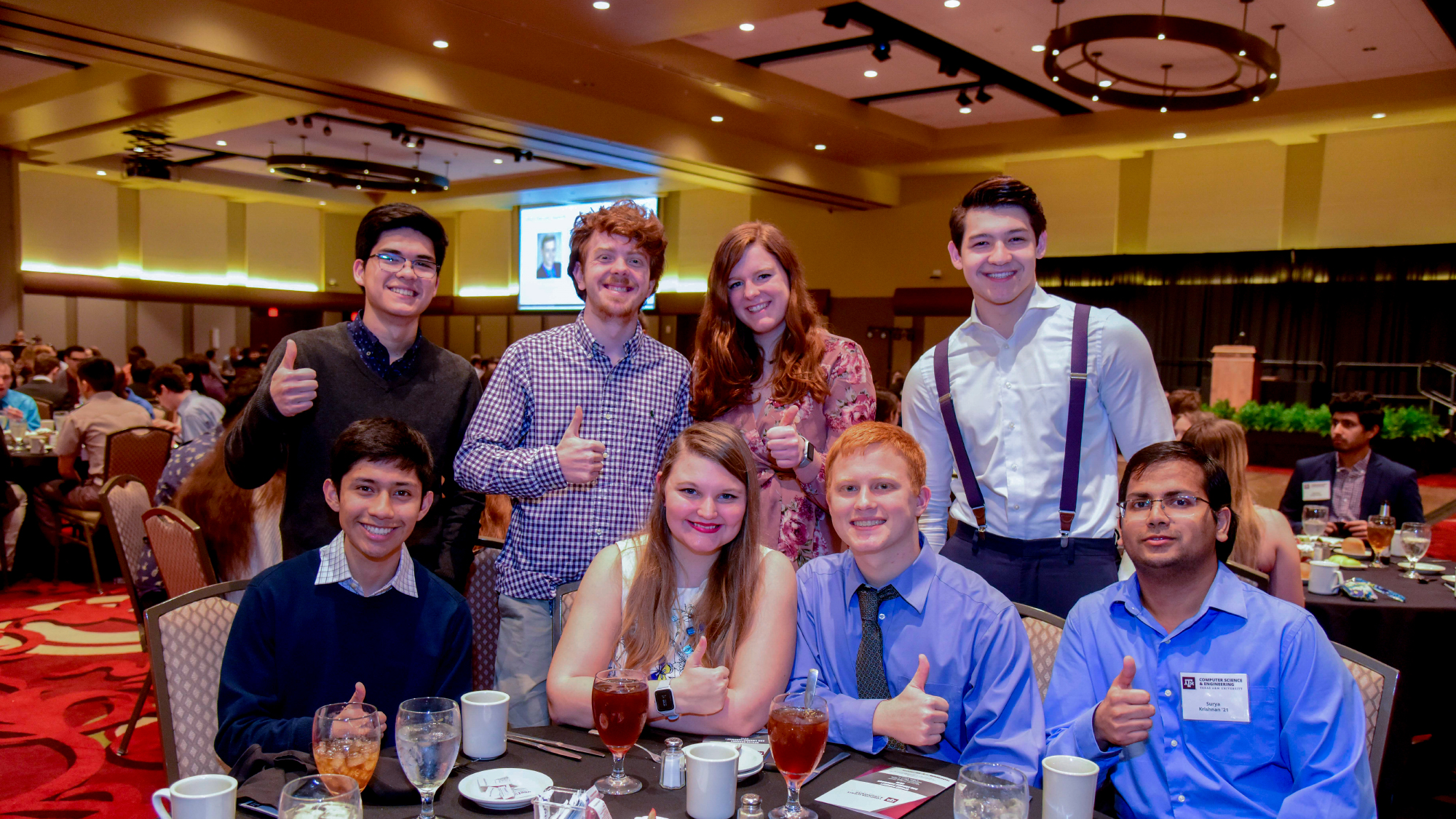 A group of students at the spring banquet dinner giving a Gig 'Em sign.