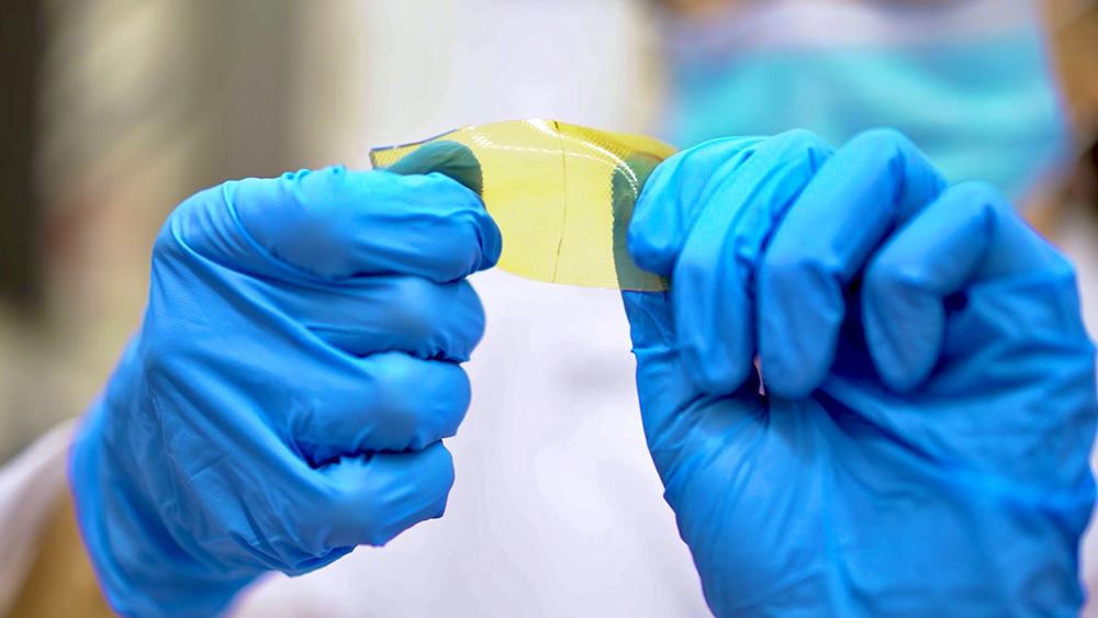 Two hands in blue latex gloves hold and twist a polymer material that is yellow and clear in color.