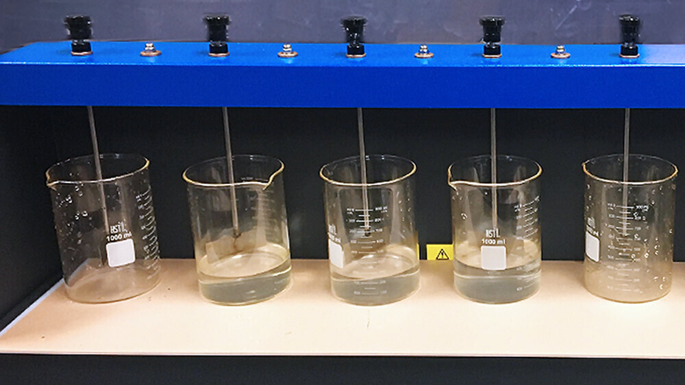 series of clear beakers, some containing fluid, lined up on machine