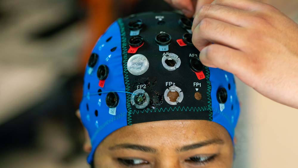 A person wearing a black and blue cloth headpiece with small, clear circular sensors.