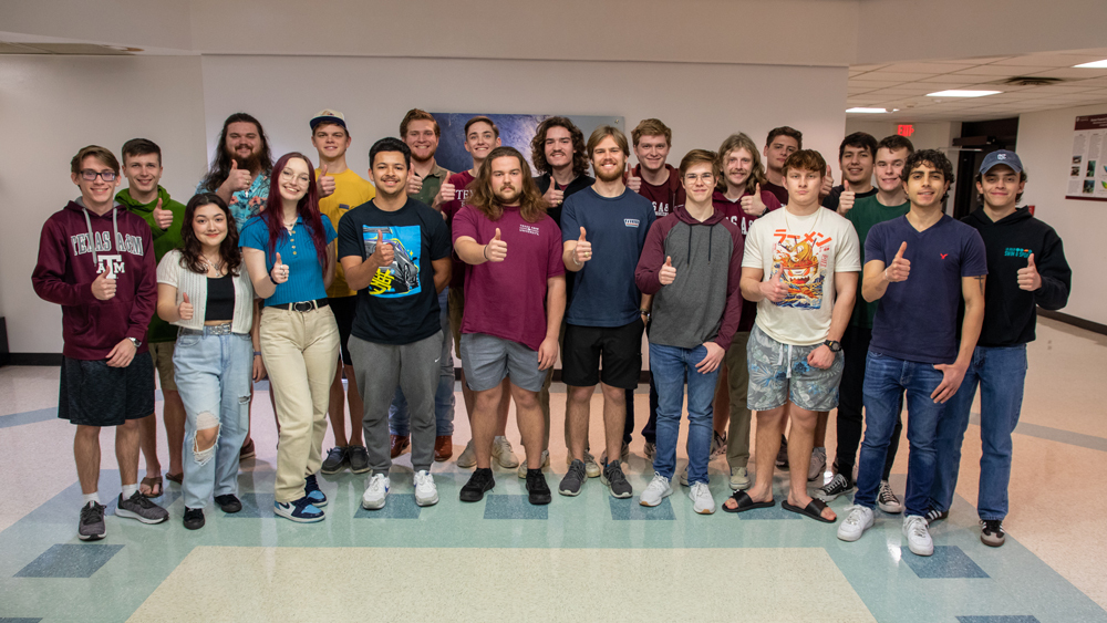 The twenty-one members of the Naval Design Team stand in the Haynes Engineering Building and give thumbs up. Team captain Ben McKeig stands in the first row, fourth from right.