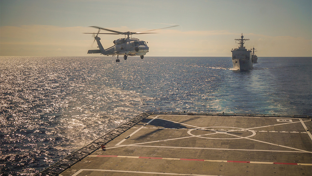 Navy helicopter landing on a ship deck out at sea.