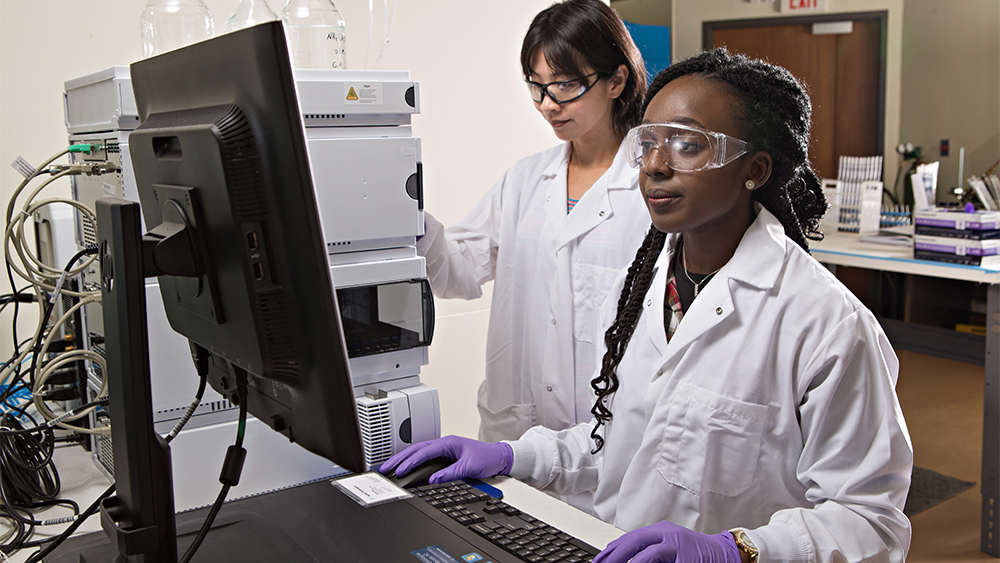 female research associate and female petroleum student reviewing lab results on computer screen