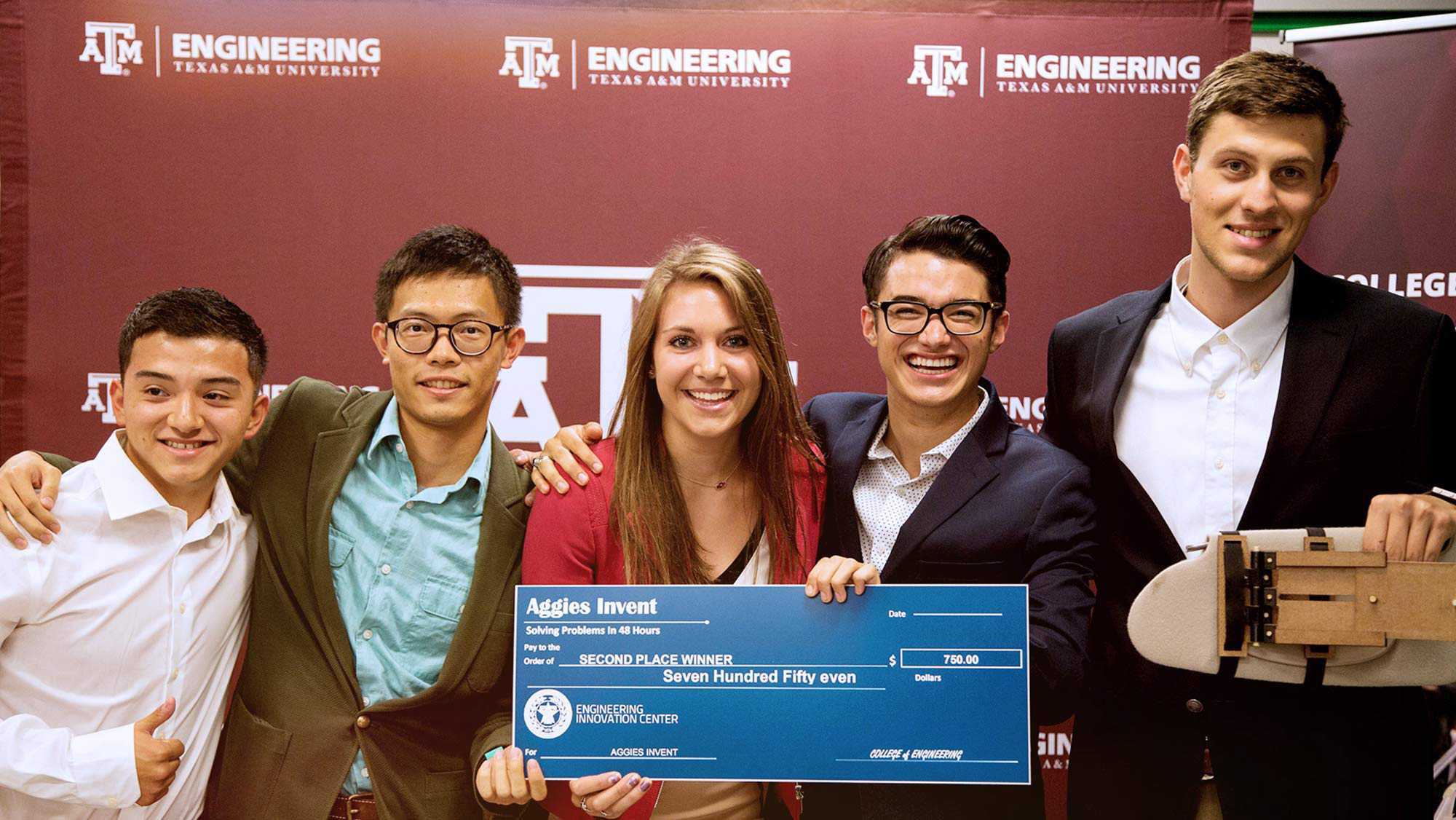 Texas A&amp;M University Engineering 5 student holding each others shoulders their project and a check Aggies Invent Solving Problems in 48 hours pay to the order of Second Place Winner Seven Hundred and Fifty Even Dollars Engineering Innovation Center.