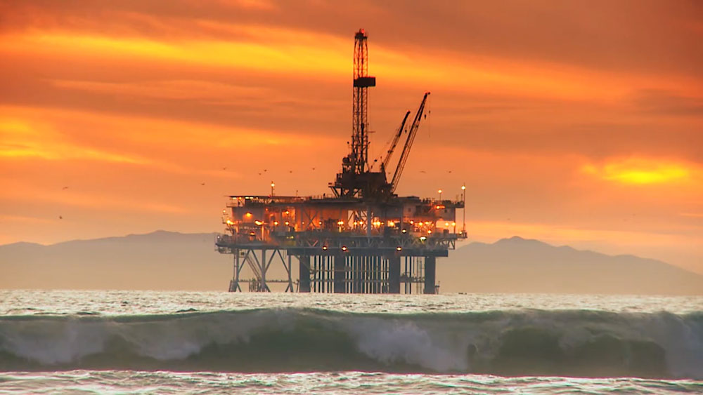offshore oil rig surrounded by ocean waves and an orange and yellow sunset in the background