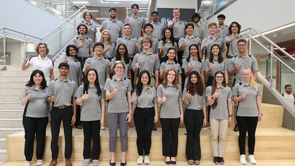 One adult and 32 student members of the 2024 Grand Challenges Scholars Program cohort standing on a set of stairs while smiling.