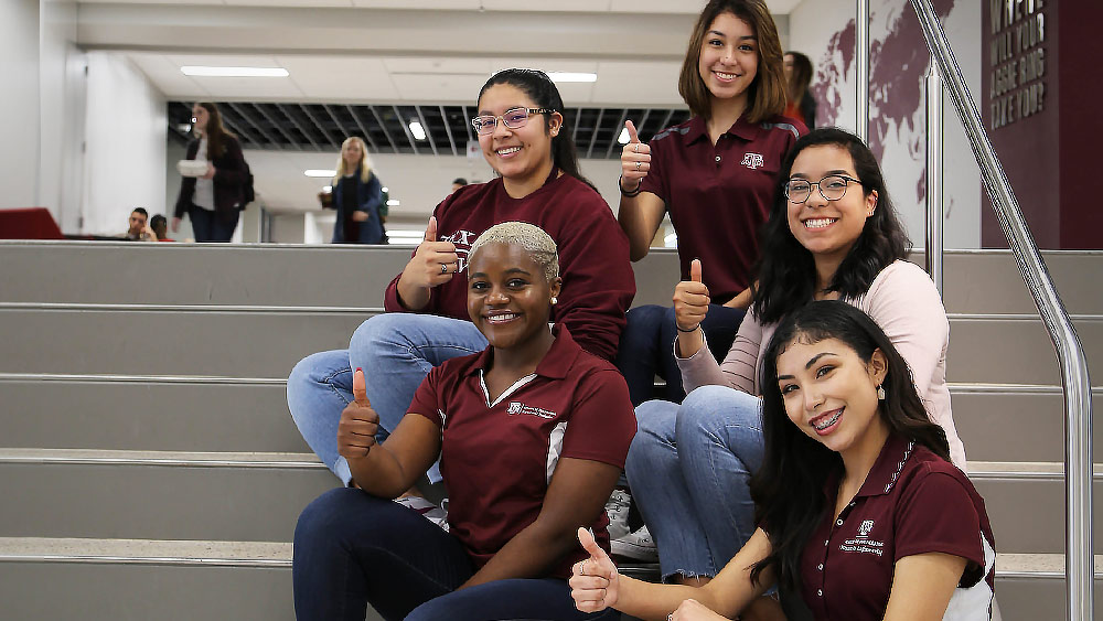 Aggie women engineering graduates holding up Gig-Em signs