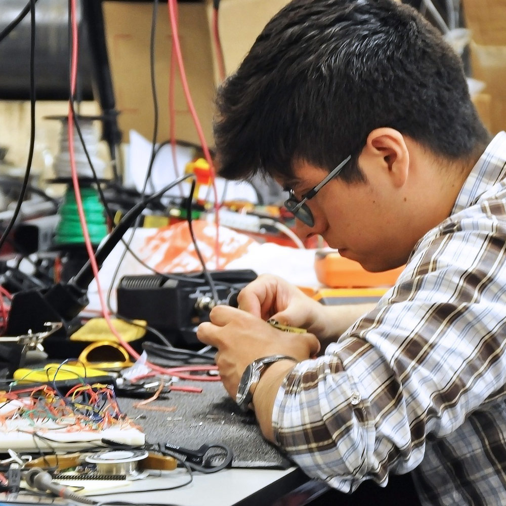 Student seated at a lab connecting wires to a piece of lab equipment.
