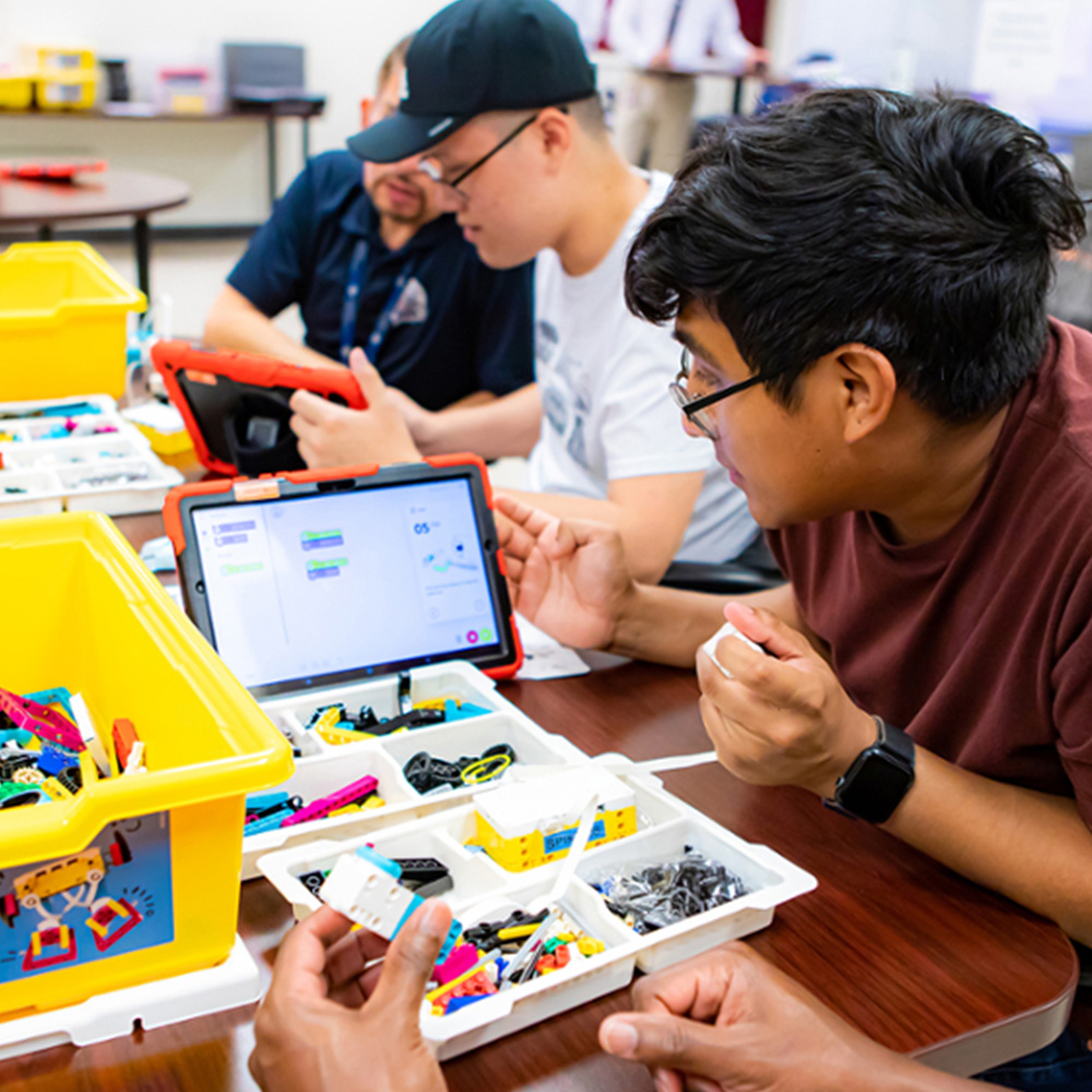 In a classroom, workshop participants interact with the robotics programming interface with Lego robotics kits on a table