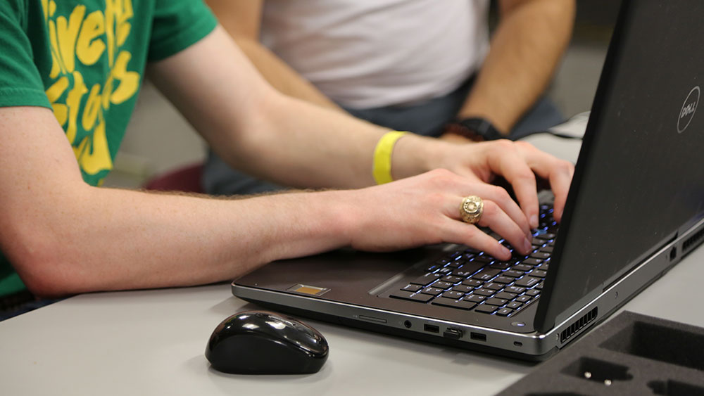 Student with Aggie ring types on a laptop