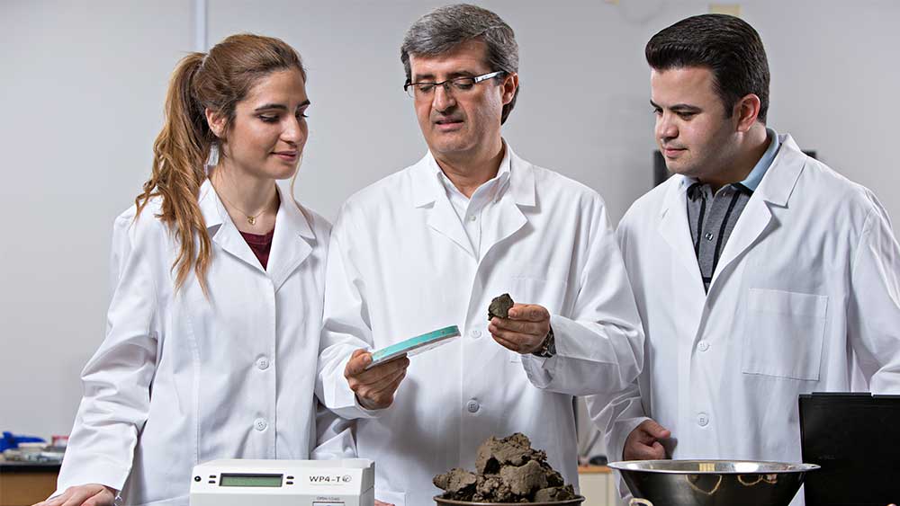 A woman and two men in lab coats measuring pieces of something brown