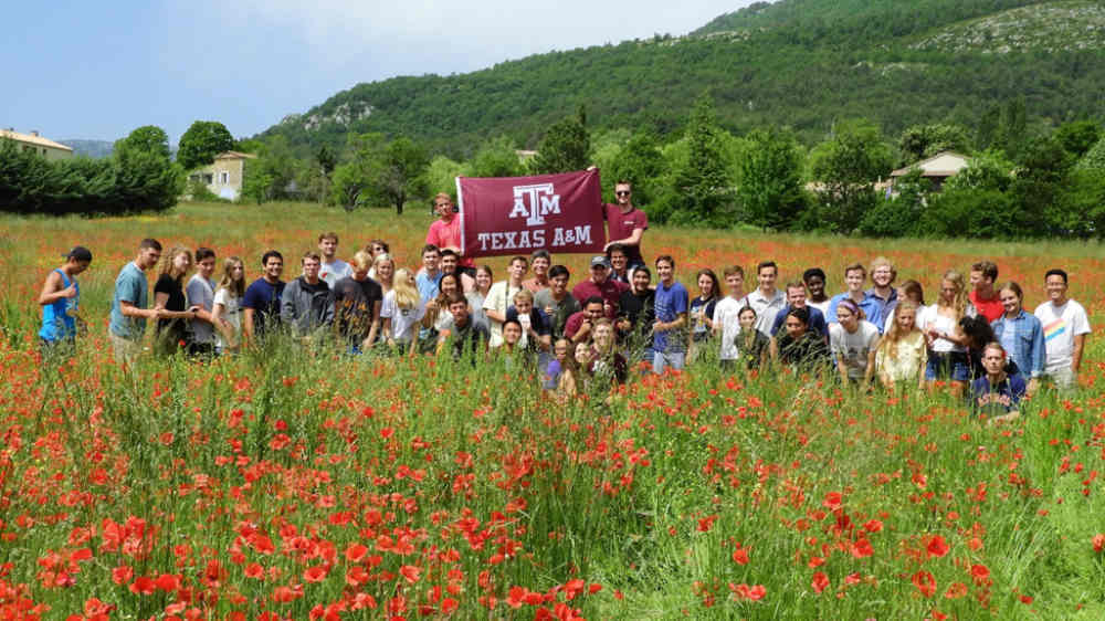 Students Hold Texas A&M Flag in a Field of Flowers. 