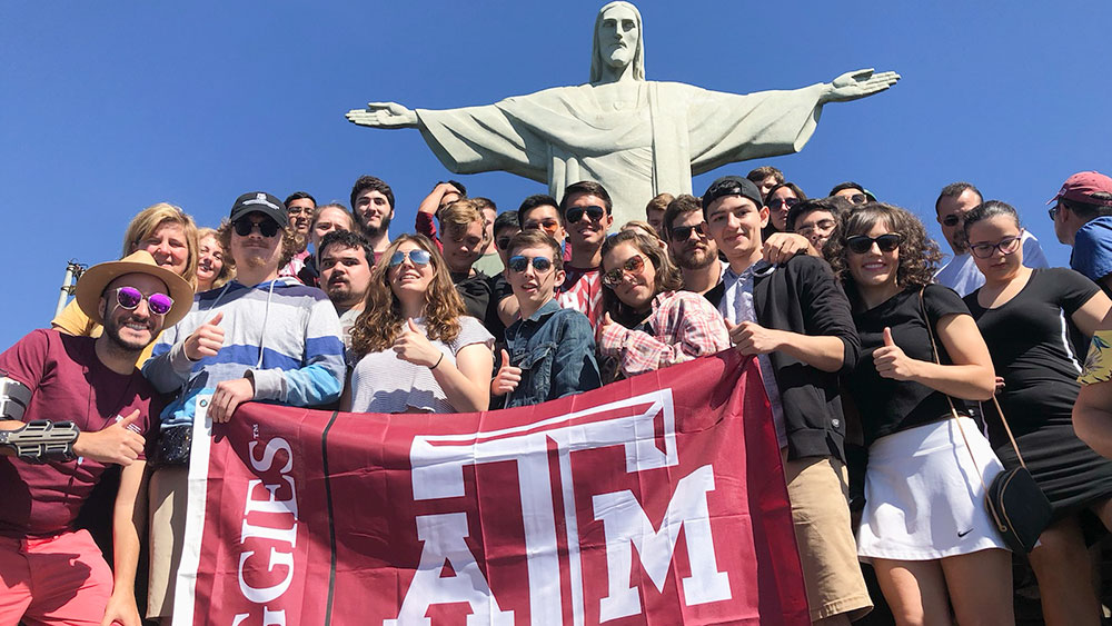 Large group of students with a large maroon Texas A&M flag standing in front of Christ the Redeemer statue in Sao Paulo, Brazil.