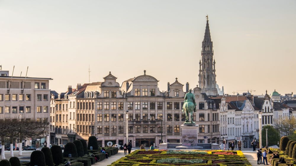 Belgium park with statue of a man riding a horse in the fore ground with building and cathedral tower in the background
