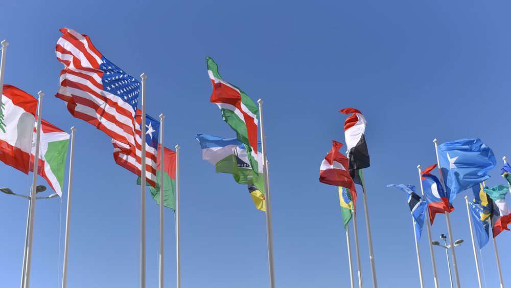 Multiple country flags waving in the blue sky.