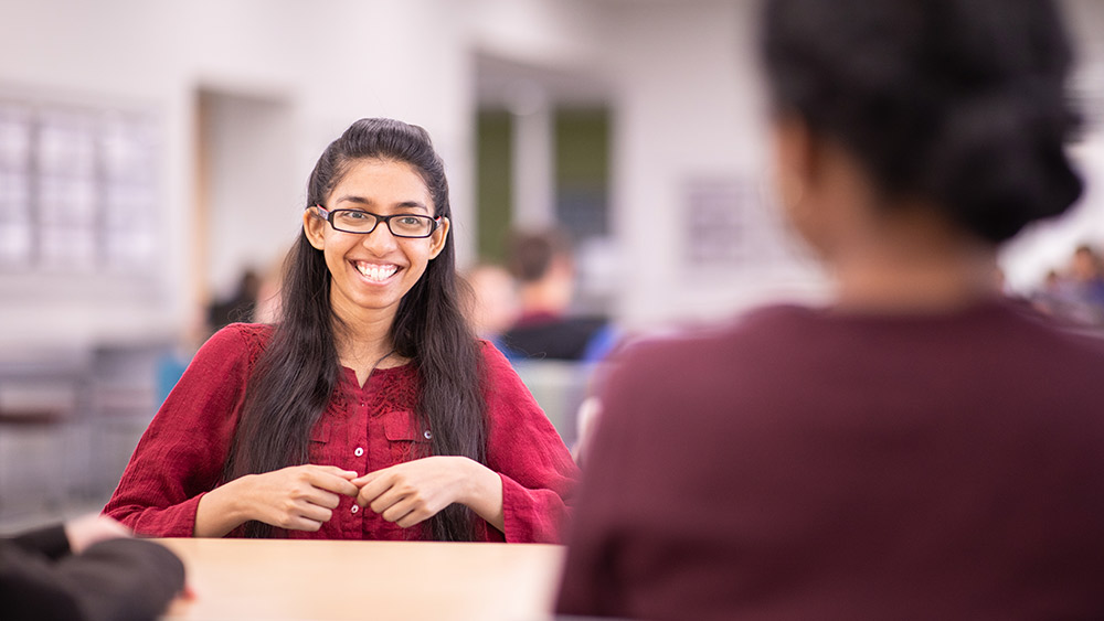 Smiling female student sitting across the table from another woman.
