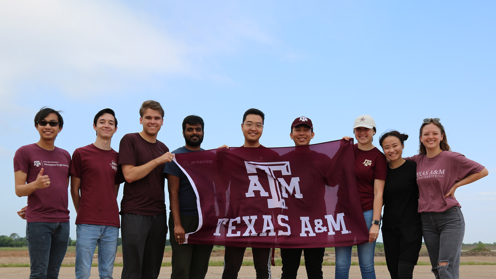 Students smiling for a photo while holding a Texas A&amp;M University flag.
