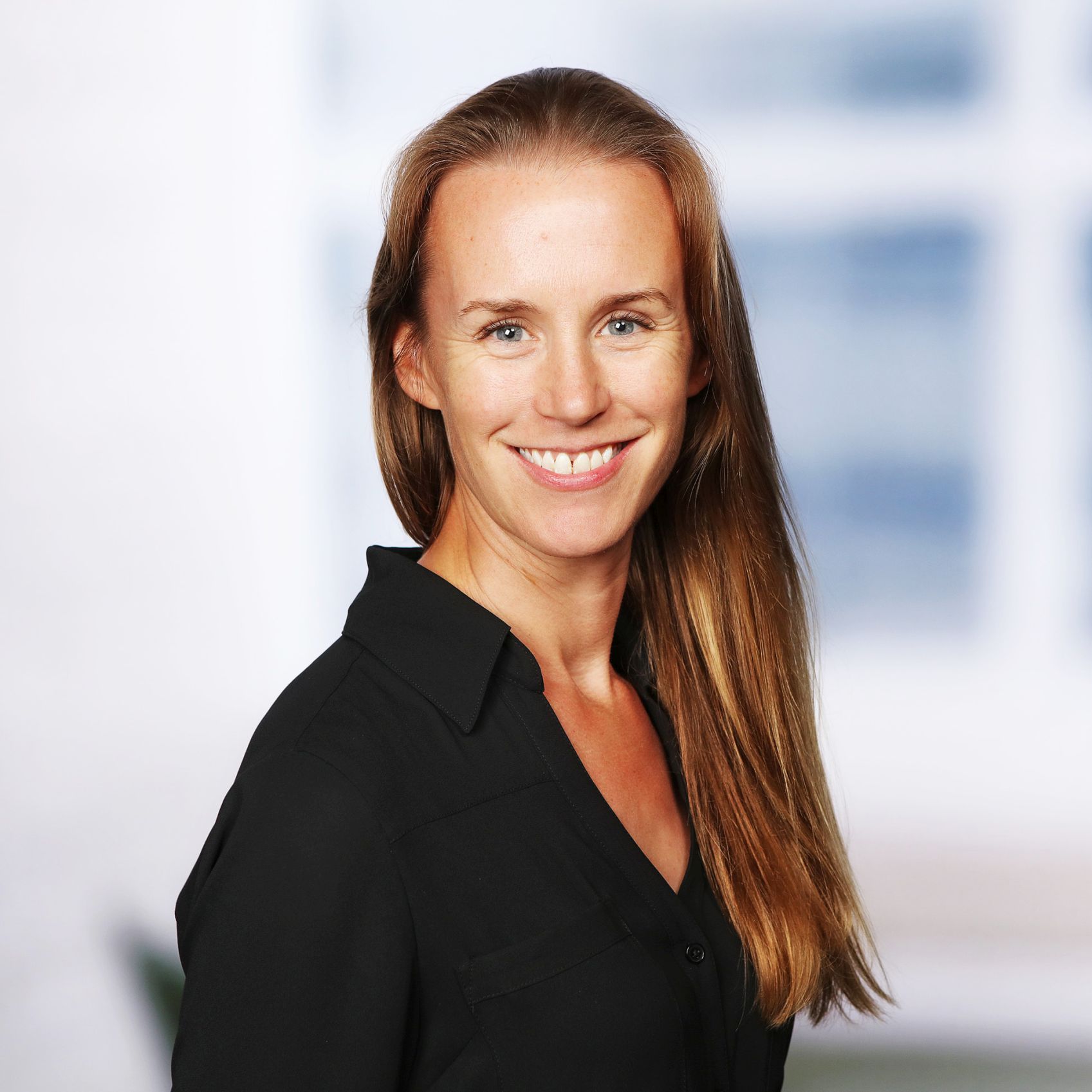 Woman with light brown hair in a black shirt in front of a blurry background