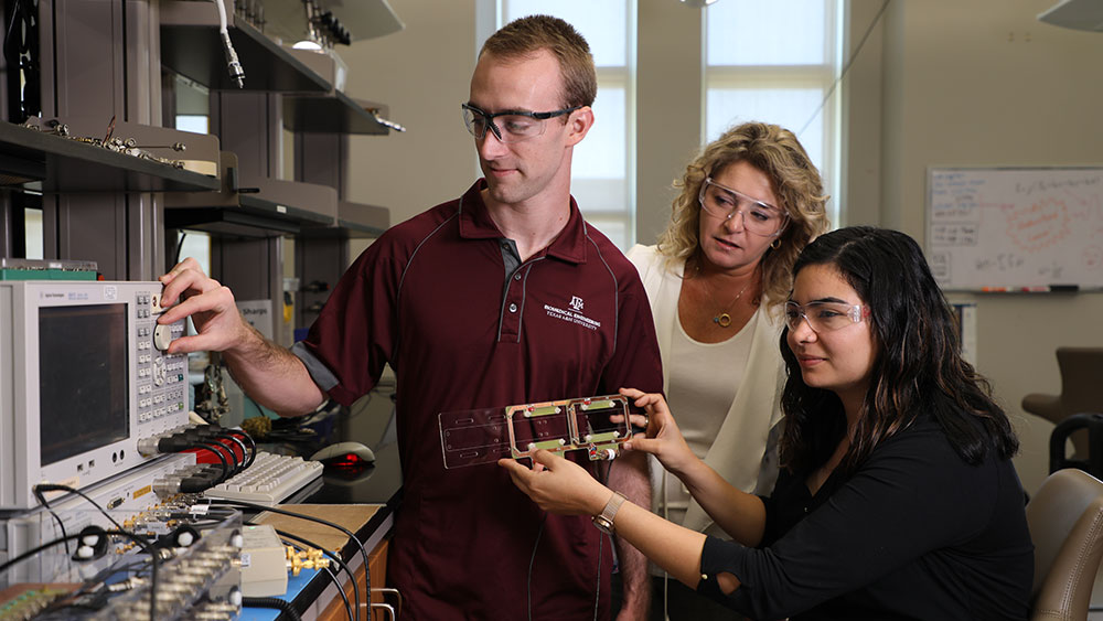 One female faculty member  stands in lab with one male student and one female student