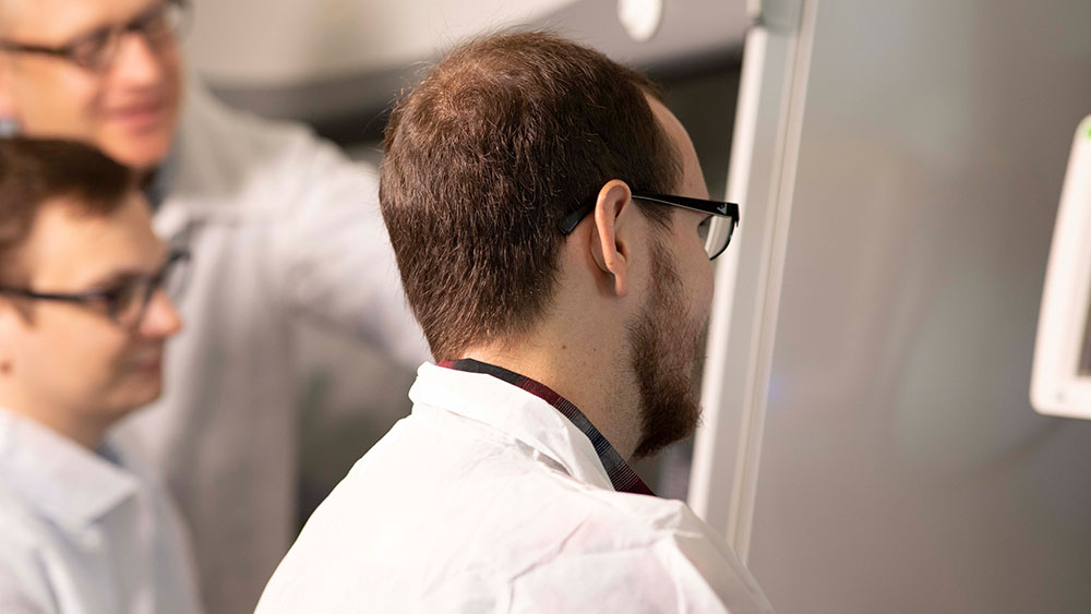 Man in white lab coat facing away