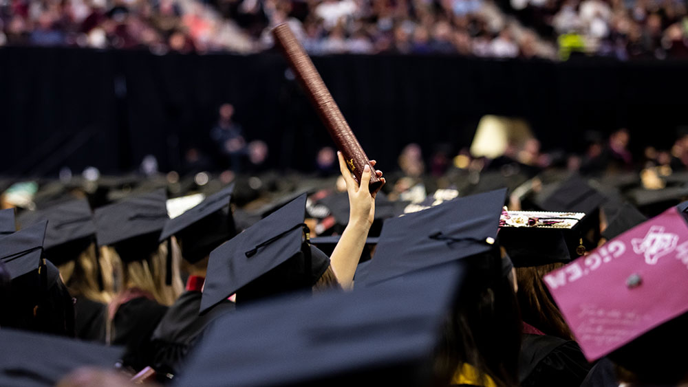Row of graduation hats in audience with hand holding up graduation tube
