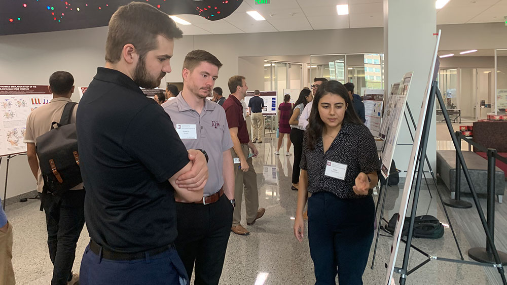 Three students standing around a poster session