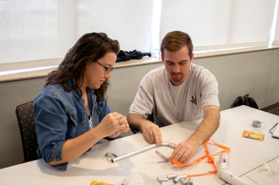 Two students, male and female, work to move aluminum ball and join pieces onto a wire.