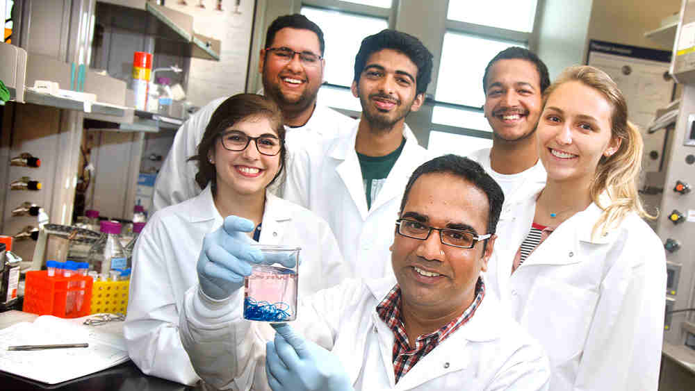 Professor and students in lab work with biomaterial in jar