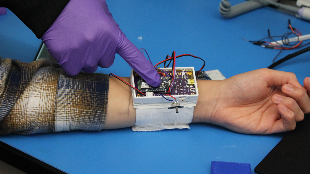 Students working with circuitry of wearable wrist device in the lab