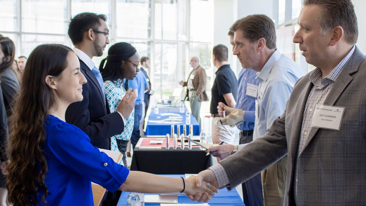 Graduate student fair booth attendee shaking hands with school representative