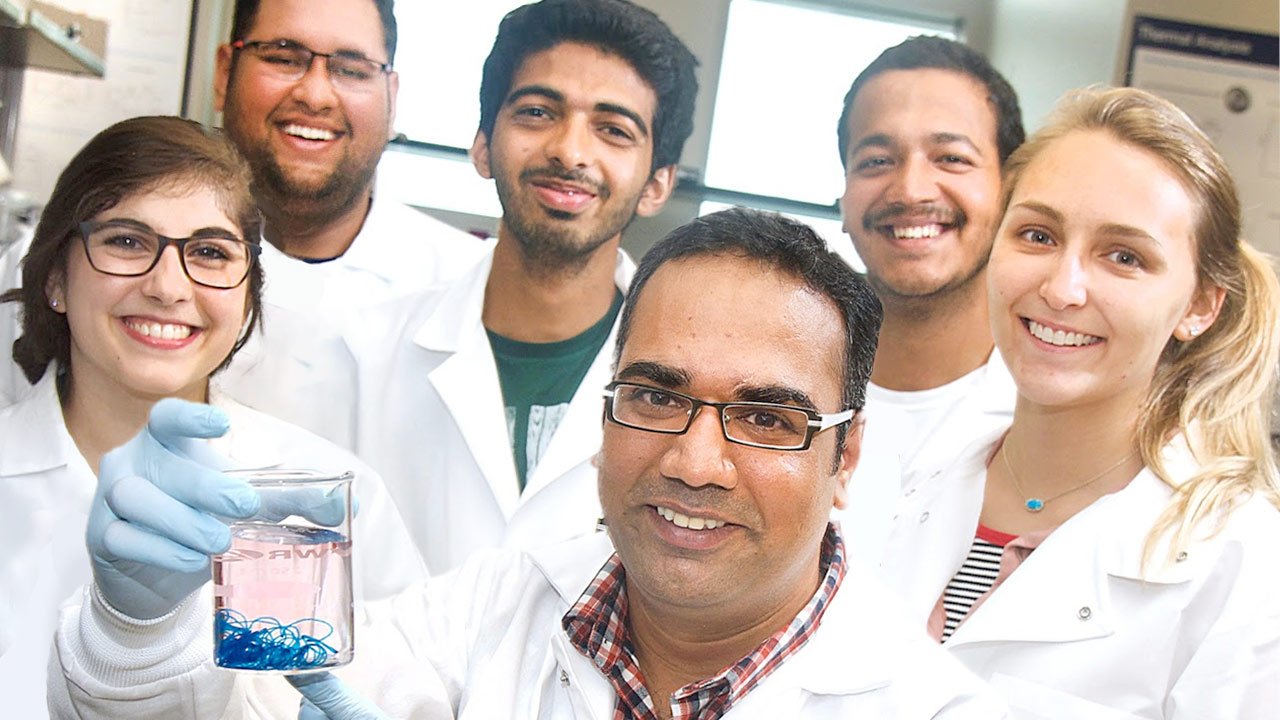 biomedical group of students in white lab coats smiling with their professor