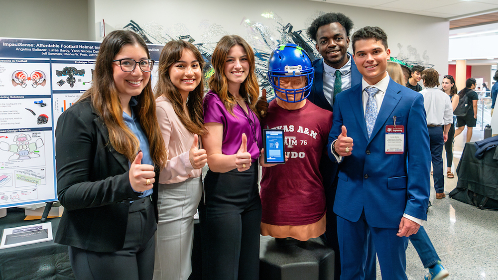 five smiling students stand with a mannequin wearing a football helmet