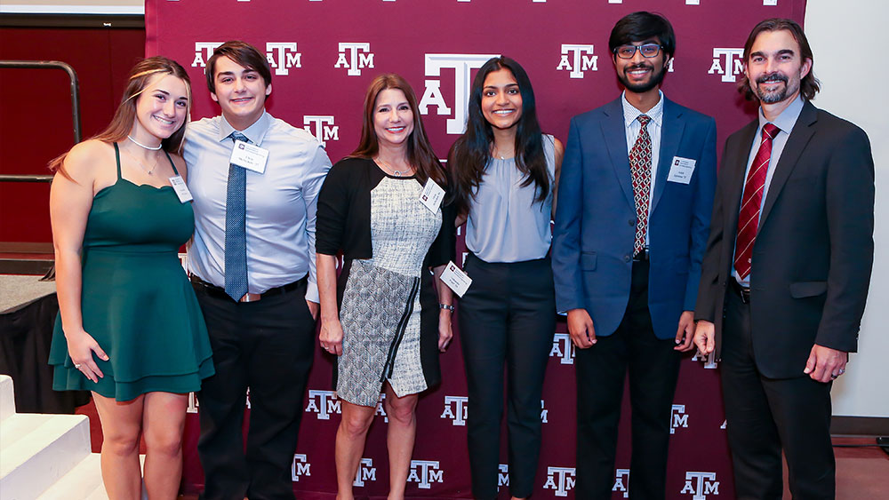 Scholarship recipients, the scholarship donor, and the biomedical engineering department head stand together in front of an A&amp;M-branded backdrop.