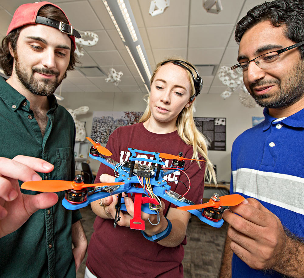 Three students looking at a drone they built.