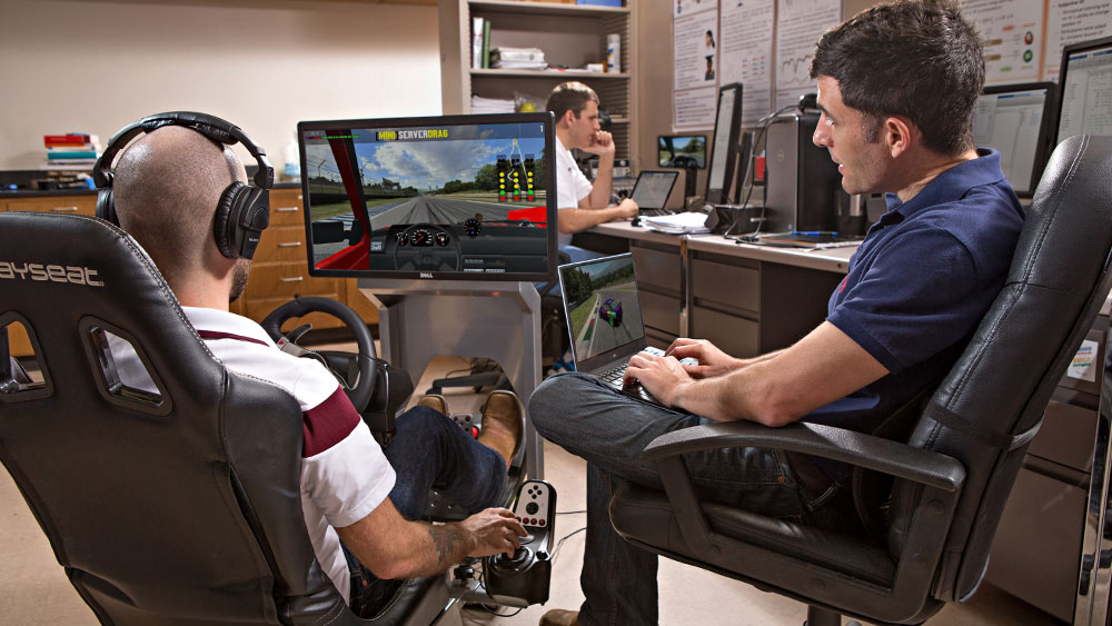 Computer engineering students engaged in a driving simulation.