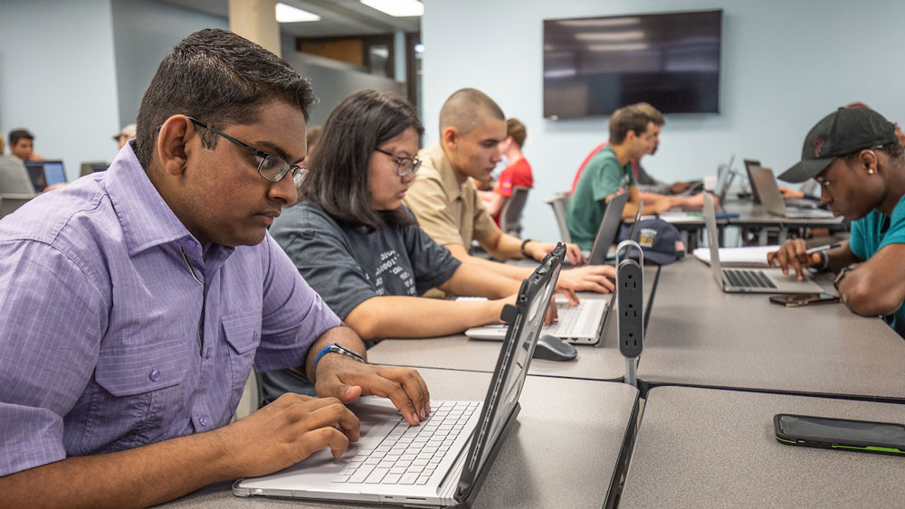 Several male and female Texas A&amp;M at Galveston students working on laptops in classroom.