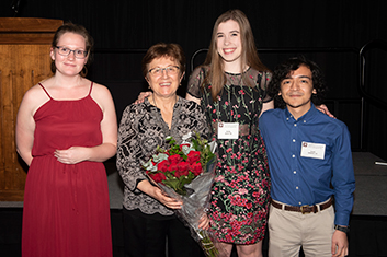 Three peer teachers standing with Dr. Leyk, who is holding a bouquet or red roses, smiling at camera.