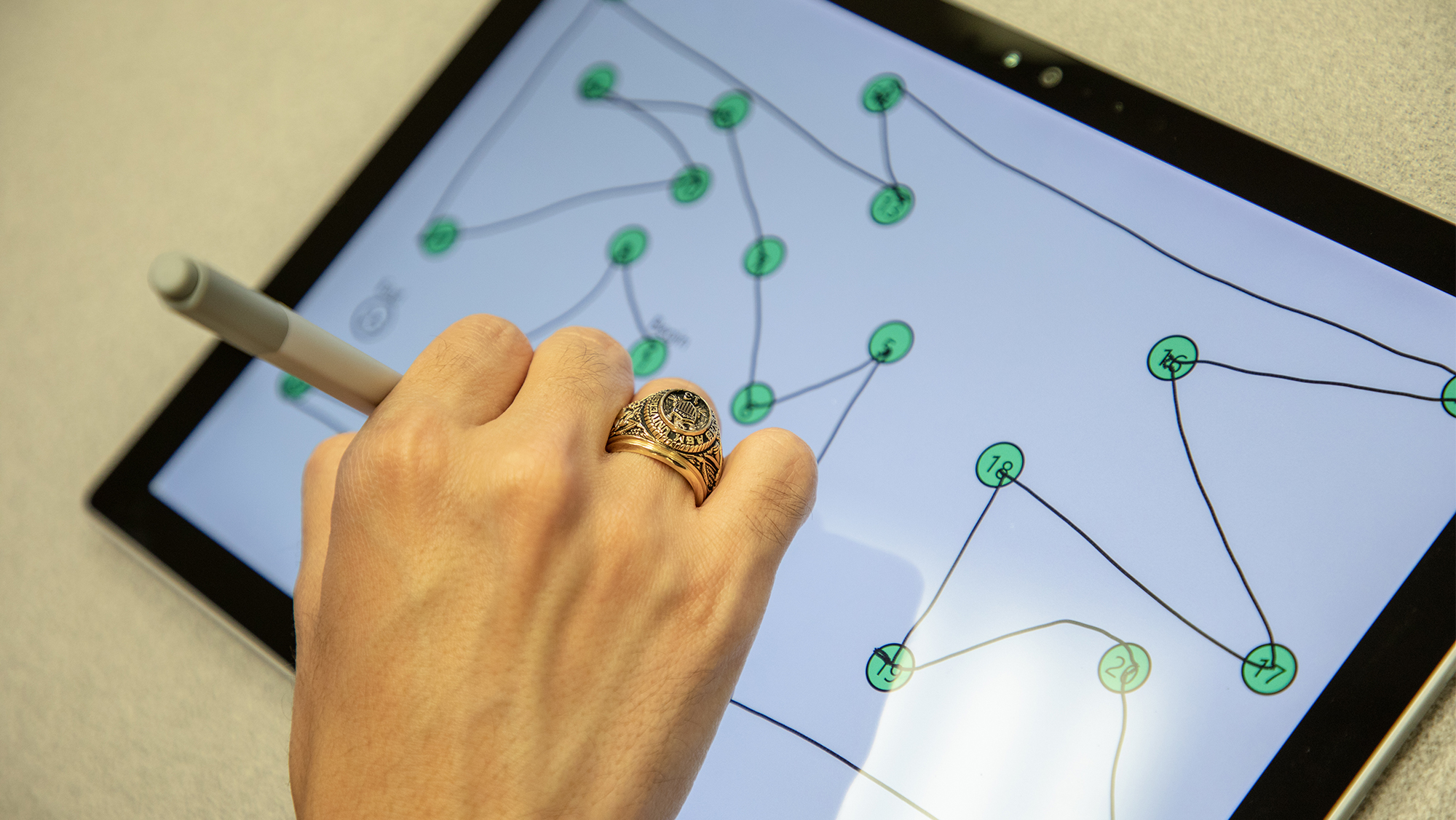 Hand using a stylus to connect numbered dots on a tablet.