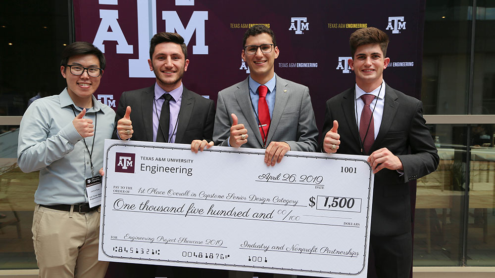 Four male students from the Engineering Project Showcase 2019 winning team holding a large check