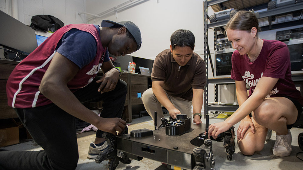 Three individuals kneel as they work on a robot.