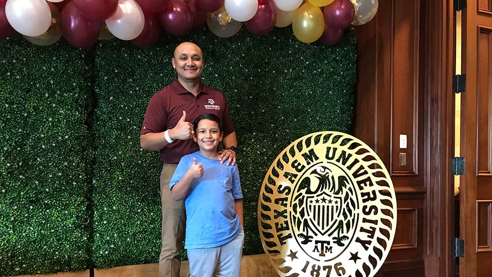 An METM student giving a gig 'em sign with his son.